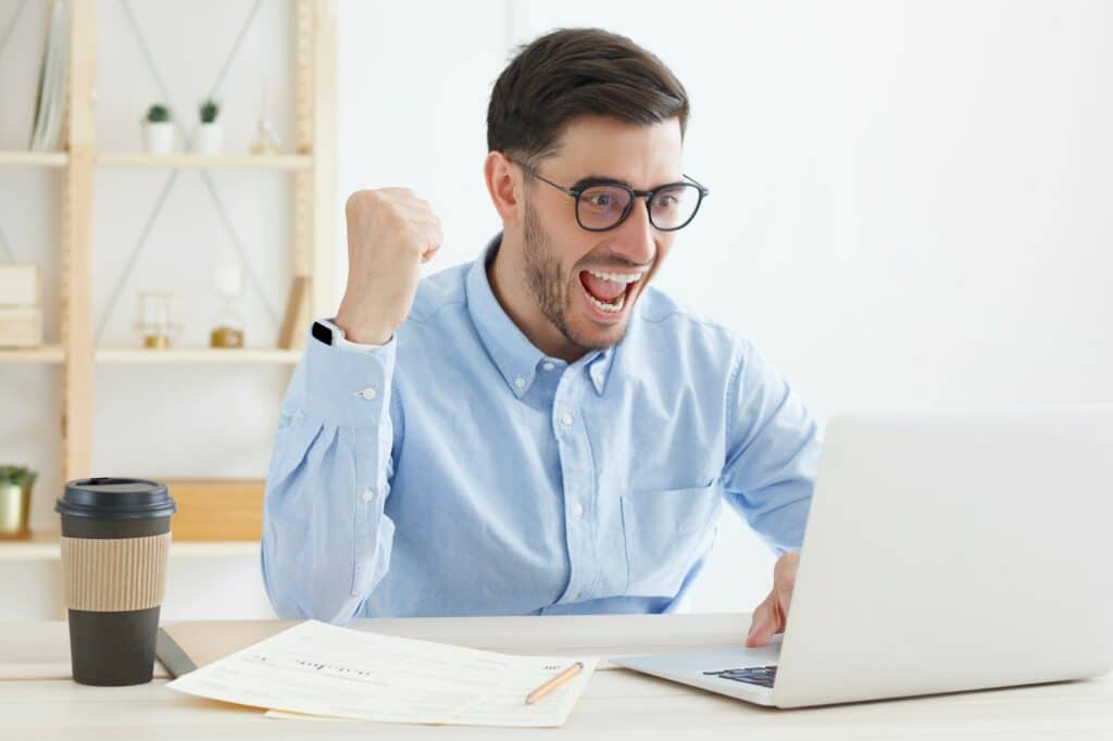 Young business man is very excited, working on laptop, celebrating his win or success in office